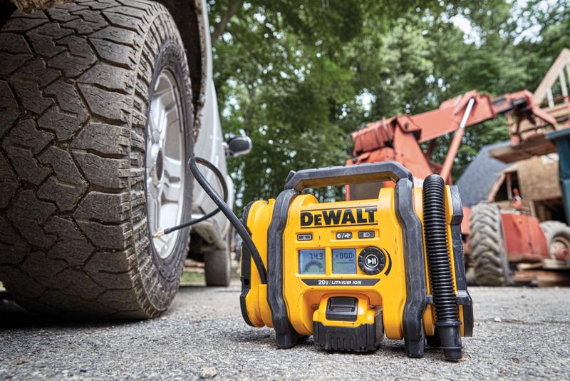 A DEWALT portable tire inflator is shown in use, connected to a vehicle tire, on an outdoor worksite with construction equipment in the background.