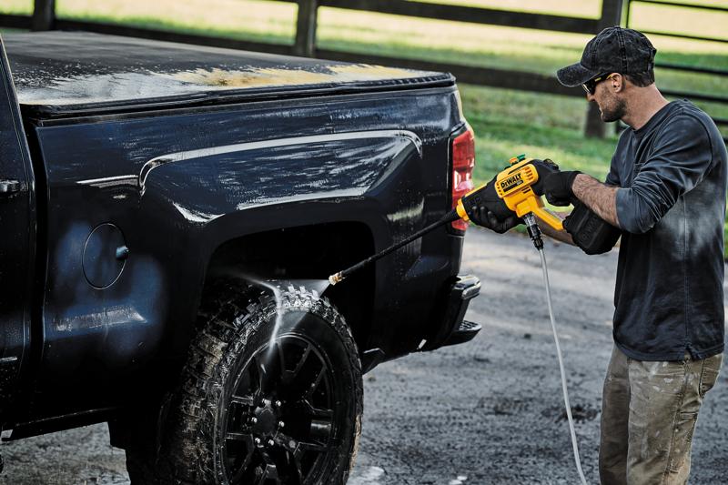 Egy személy DEWALT DCPW550B vezeték nélküli magasnyomású mosót használ egy fekete pickup teherautó kereke és oldala tisztításához a szabadban.
